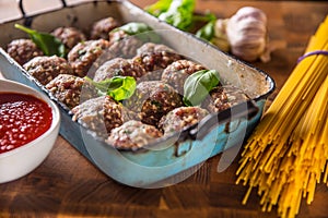 Raw feef meat balls basil tomato sauce garlic and spaghetti on butcher board