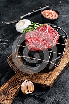 Raw fillet mignon beef steak on a grill with herbs. Black background. Top view