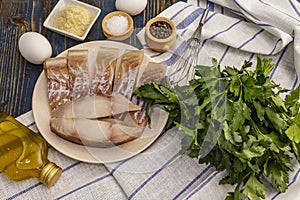 Raw fillet of saithe and frying ingredients. Fresh slices on a plate, spices, eggs, oil, breadcrumbs, parsley photo