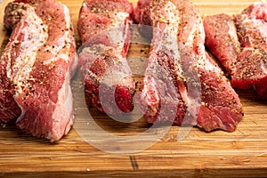 Raw fillets of pork meat freshly seasoned on top of a wooden kitchen board close up shot