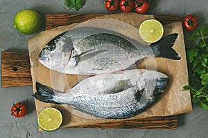 Raw fish on a cutting board with cherry tomatoes, parsley and lime. Top view.