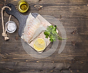 Raw fish fillet on a cutting board with lemon, herbs, butter and salt border ,place for text wooden rustic background top view