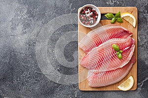 Raw fish fillet of tilapia on a cutting Board with lemon and spices. Dark table with copy space