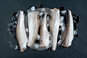 Raw fish hake. Five Raw fish fillet on ice on dark background photo