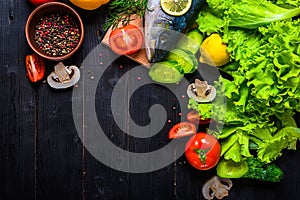 Raw fish and ingredients: lemon, spices, greens, tomato, on a wooden table, top view.