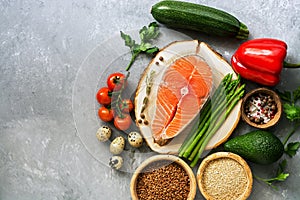 Raw fish steak salmon, cereals, fresh vegetables, quail egg, nuts and spices on a gray background. Healthy balanced food. Flat lay