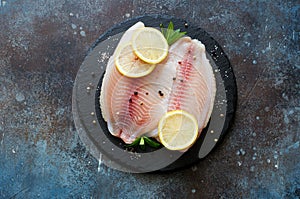 Raw fish tilapia fillet with spices and lemon slices