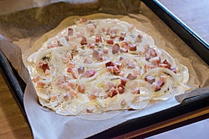 Raw flammkuchen with onion and bacon on the top