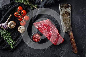 Raw, flap or flank, also known Bavette steak near butcher knife with pink pepper and rosemary. Black background. Top view