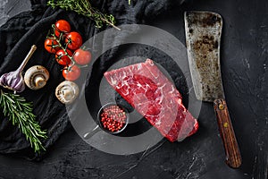 Raw, flap or flank, also known Bavette steak near butcher knife with pink pepper and rosemary. Black background. Top view photo