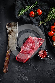 Raw, flap or flank, also known Bavette steak near butcher knife with pink pepper and rosemary. Black background. Top view vertical photo