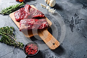 Raw flap steak flank cut with Machete, Skirt Steak, on woods chopping board, with herbs tomatoes peppercorns over grey stone