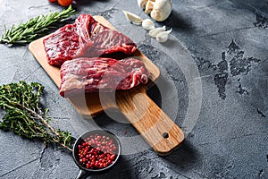 Raw flap steak flank cut with Machete, Skirt Steak, on woods chopping board, with herbs tomatoes peppercorns over grey stone photo