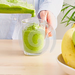 Raw foodism, green smoothie with banana and spinach. Woman pouring detox drink from blender