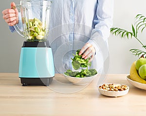 Raw foodism, green smoothie with banana and spinach. Woman putting spinach leaves to blender