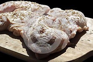 Raw free range organic chicken breasts covered with rosemary on a chopping board