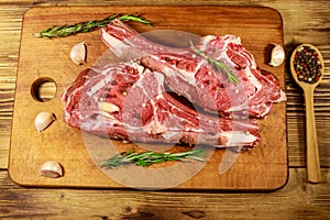 Raw fresh beef rib eye steak on bone with spices, garlic and rosemary on wooden table. Top view