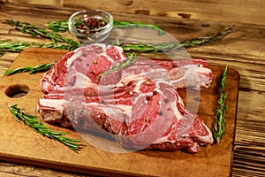 Raw fresh beef rib eye steaks on bone with spices and rosemary on wooden table