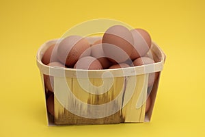 Raw, fresh chicken eggs in a basket. Brown eggs in a basket on a light, yellow background. Copy space