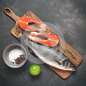 Raw fresh fish sea bass and trout on a cutting board, dark grunge background. Top view, flat lay.