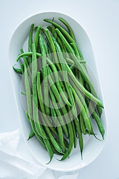Raw fresh green beans on white plate, white background