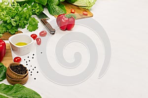 Raw fresh green vegetables, greens, red cherry tomatoes and kitchenware on soft white wood board, border.