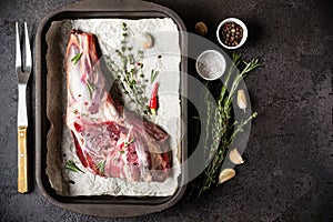 Raw fresh Lamb Meat in baking tray, herbs and fork on black stone background