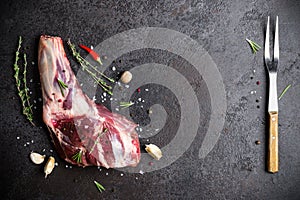 Raw fresh Lamb Meat shank, herbs and fork on black stone background
