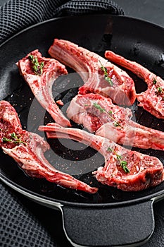Raw fresh lamb rib chops with salt, pepper and herbs in a pan. Black background. Top view