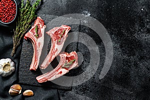 Raw fresh lamb ribs with pepper and rosemary. Organic meat. Black background. Top view. Copy space