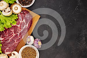 Raw fresh marble meat steak and seasonings on a dark marble background, top view