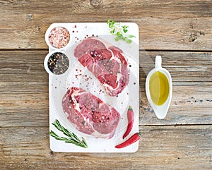 Raw fresh meat Ribeye steak entrecote and seasonings on white cutting board over grunge background.