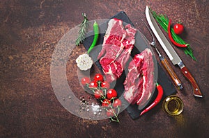 Raw fresh meat steak with cherry tomatoes, hot pepper, garlic, oil and herbs on dark stone, concrete background. Banner.