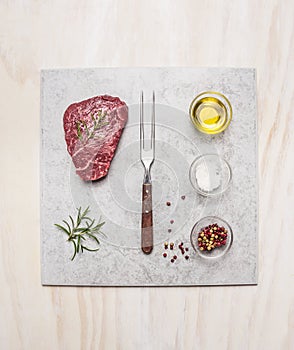 Raw fresh meat Steak with spice ingredients on light marble plate over wooden background, top view