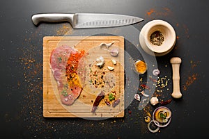 Raw fresh pork meat on board with condiments on dark background