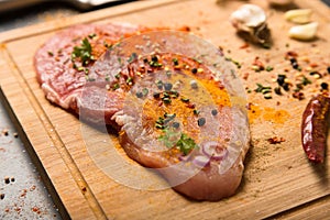 Raw fresh pork meat on board with condiments on dark background