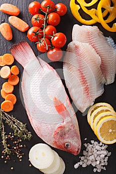 Raw fresh red tilapia and vegetables, spices close-up on a black