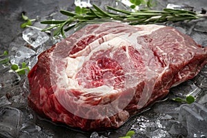 Raw fresh rib eye beef steak on ice with herbs