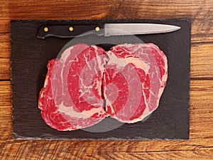 Raw fresh rib eye steaks on a dark slate plate.