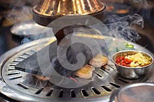 raw fresh sliced pork on hot pan and chili garlic with range hood smoke Korean-Style BBQ in a Korean restaurant.
