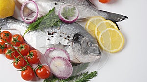 Raw fresh uncooked dorado or sea bream fish with lemon, herbs,  cherry tomatoes and spices on white background
