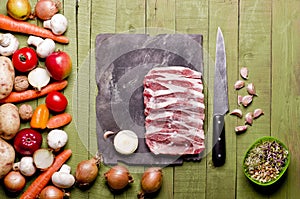 Raw frozen meat on green wooden background. Pork neck raw, vegetables close-up on a slate board. Copy space