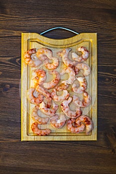 Raw frozen prawns laid out on a cutting board on a wooden table