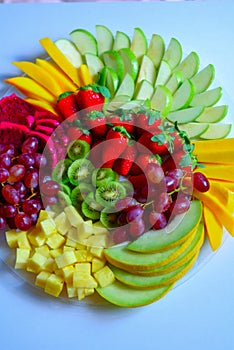 Raw fruits assortment platter on the white plate, on the white table.