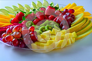 Raw fruits assortment platter on the white plate, on the white table.