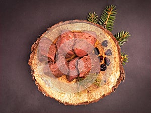 Raw game meat, beef on chopping block, wood slice. Steaks, pieces of red meat on wood, on black stony background. photo