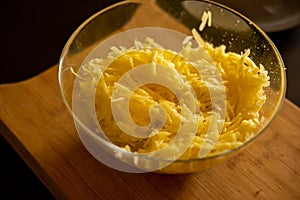 Raw grated potato on wooden cutting board in glass bowl close up