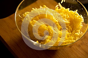 Raw grated potato on wooden cutting board in glass bowl closeup