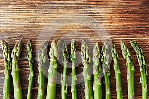 Raw green asparagus stems in a row at the bottom line on a rustic wooden table.