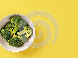 Raw green broccoli florets in a bowl against yellow background. Vitamin vegetarian food recipe. Concept of cooking low calorie